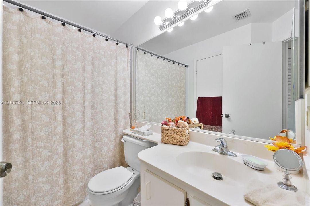 Bathroom featuring an integrated vanity countertop with an oval basin, a large wall-mounted mirror, and multi-bulb Hollywood-style light fixture