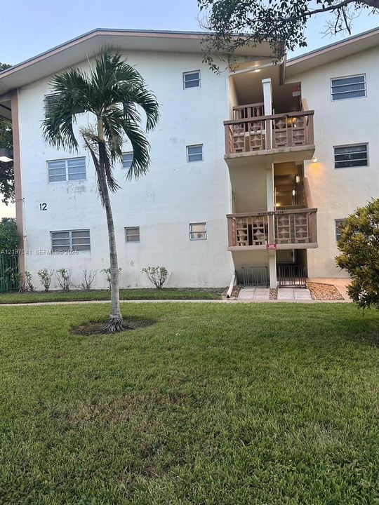 Three-story building exterior featuring stucco siding, jalousie windows, and decorative concrete screen railings on balconies