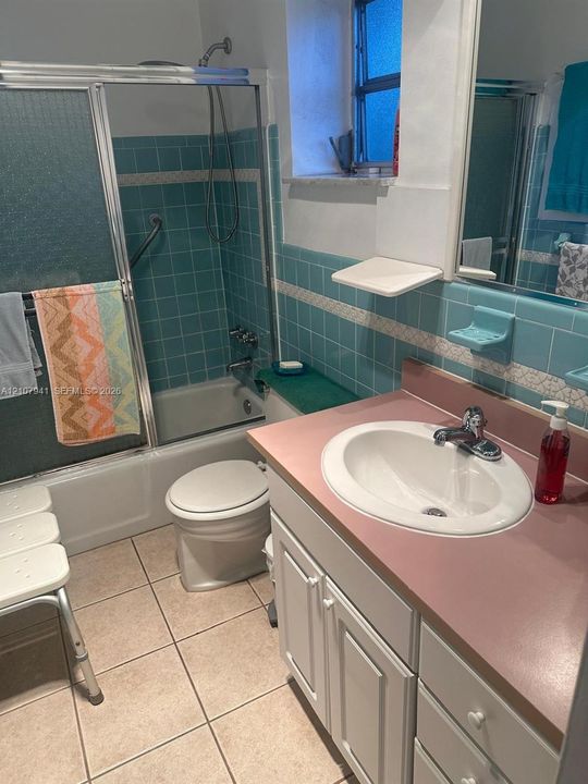 Bathroom featuring a vanity with a solid-surface countertop and integrated sink, a tiled bathtub surround with accent inlay, and large-format floor tiling