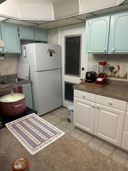 Kitchen featuring two-tone cabinetry, solid surface countertops, tile backsplash, and a double-basin stainless steel sink