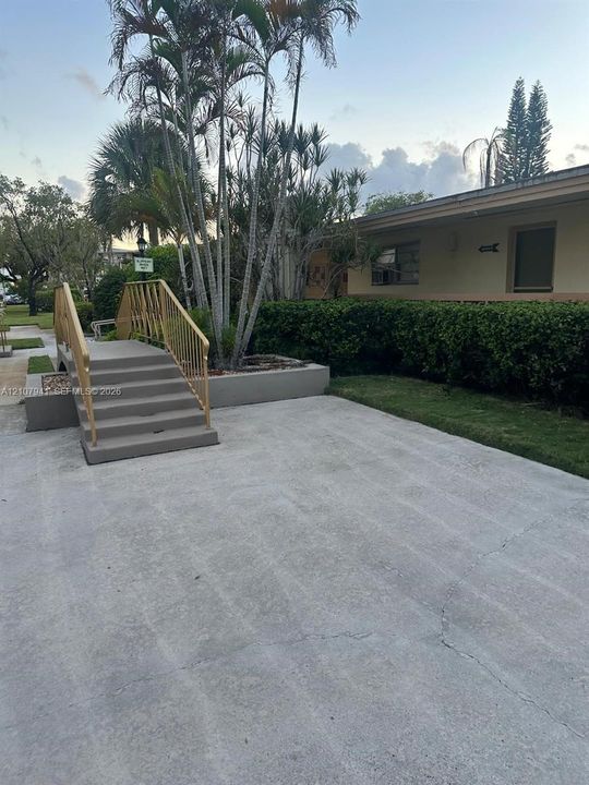 Concrete walkway with metal railings, mature palm trees, raised masonry planter, and landscaped shrubbery