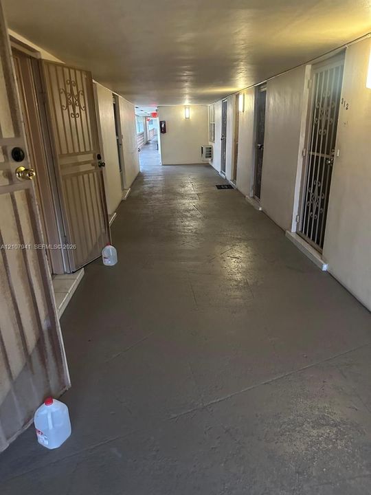 Covered exterior corridor featuring concrete flooring, wall-mounted light fixtures, and decorative metal security screen doors