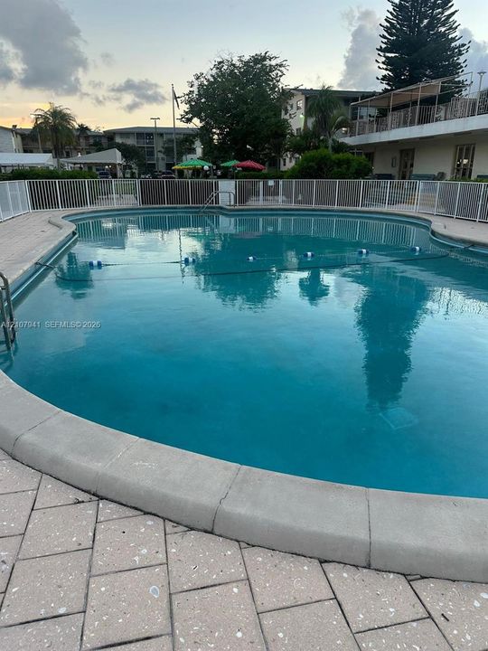 In-ground swimming pool with stone-style paver decking, white perimeter fencing, and stainless steel ladder