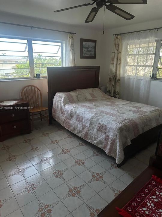 Bedroom featuring patterned tile flooring, dual louvered windows, and a ceiling fan with integrated lighting