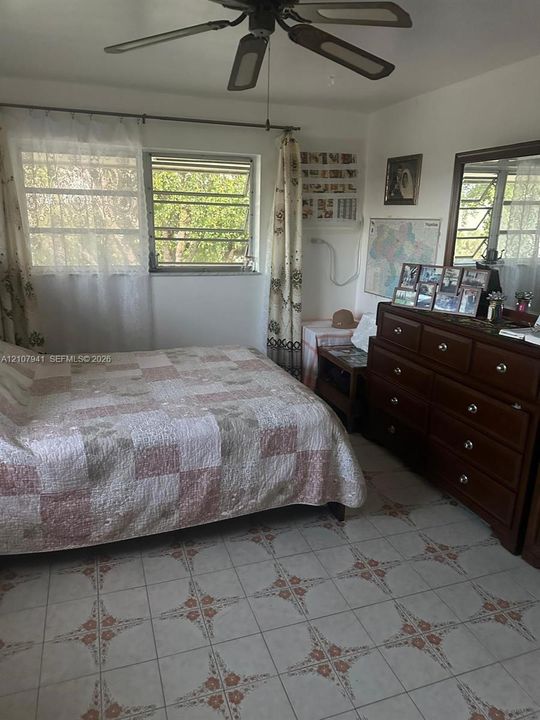 Bedroom featuring patterned ceramic tile flooring, horizontal window security bars, and a ceiling-mounted fan