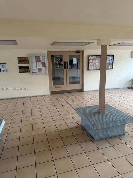 Covered entrance featuring tile flooring, double glass-paneled doors, and a central structural column with a stone-finish masonry base