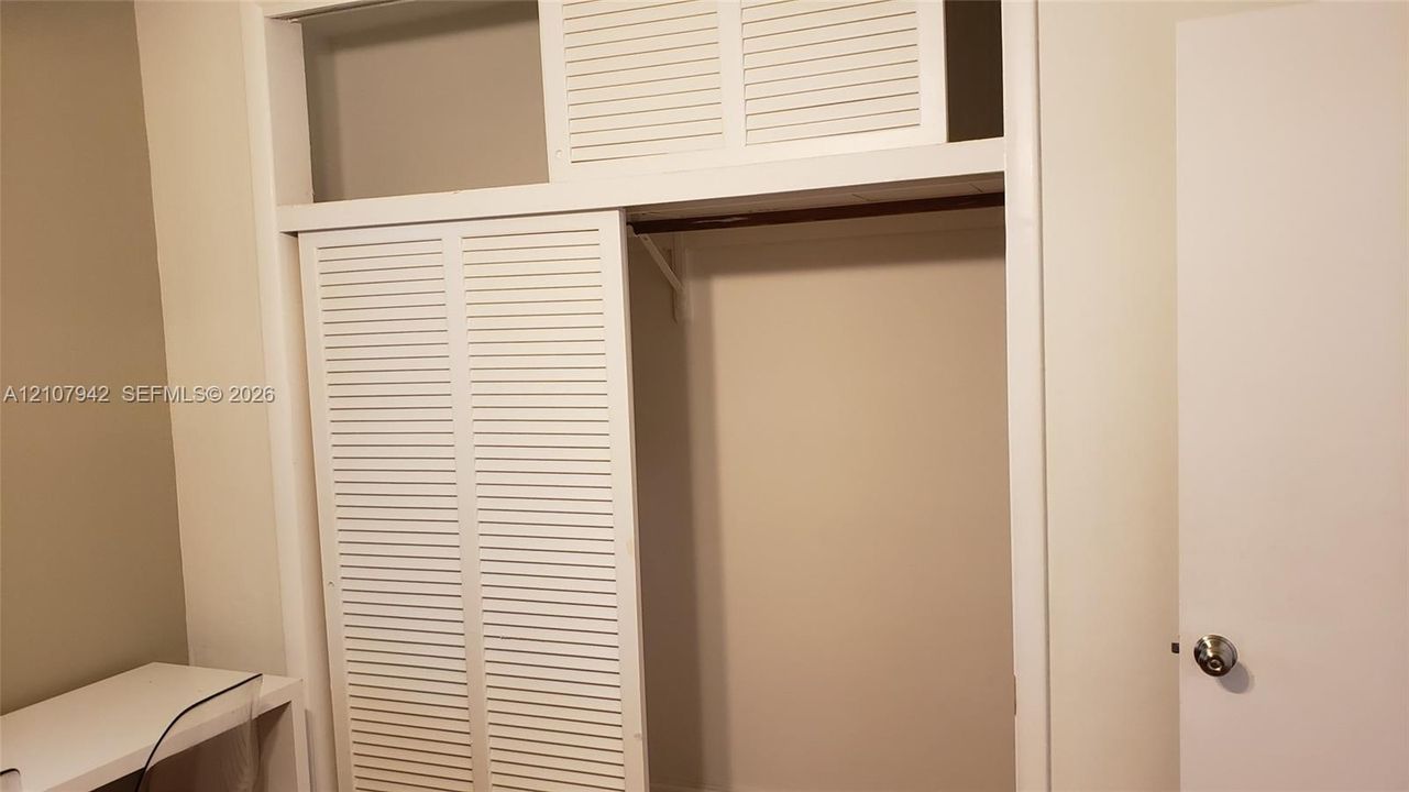 Storage closet featuring white louvered sliding doors, upper transom storage panels, and a built-in hanging rod