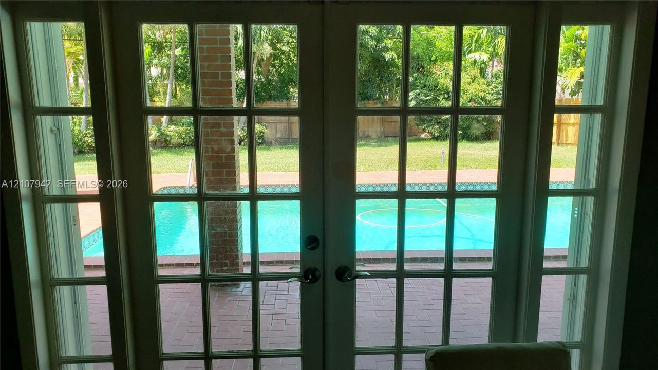 French-style multi-pane glass double doors with sidelights, brick-paved patio, and swimming pool