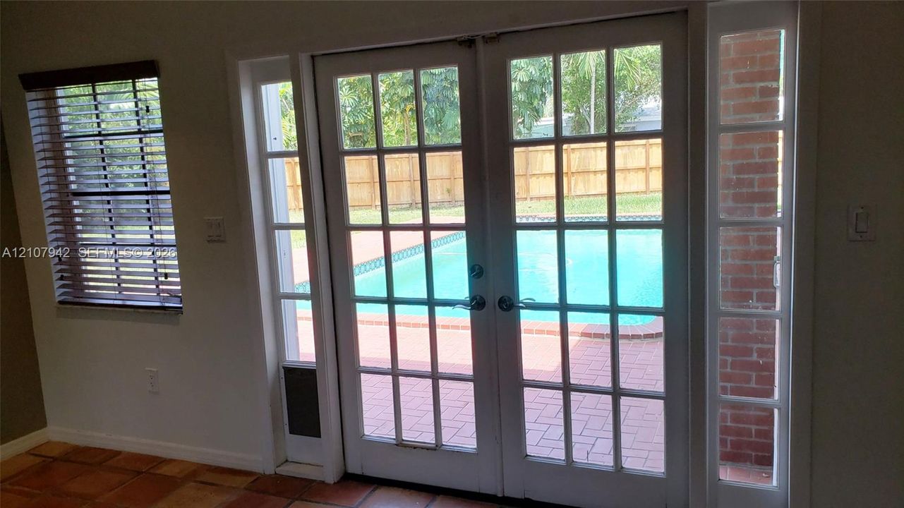 Multi-light French doors with sidelights, red brick masonry accents, and ceramic tile flooring, featuring exterior access to a paved pool deck