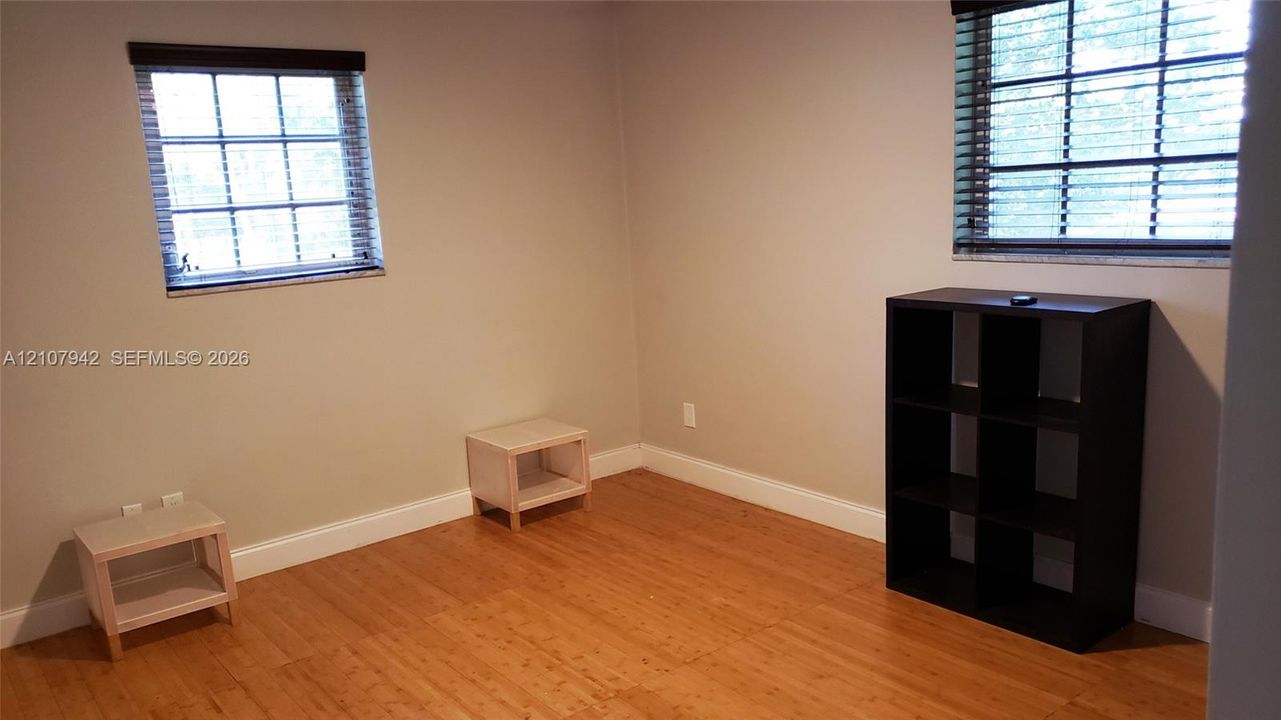 Room featuring wood-finish flooring, neutral wall paint, and two grid-pattern windows with integrated blinds