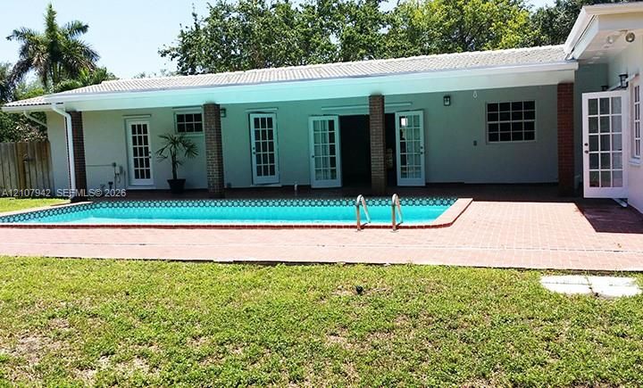 Exterior features include a covered patio with brick columns, a rectangular inground pool, red brick pool decking, and multiple sets of glass-paned doors