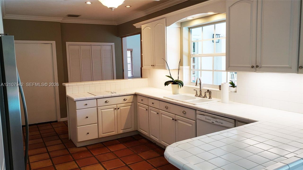 Kitchen featuring white cabinetry, tile countertops, tile flooring, a dual-basin sink with a metallic faucet, and under-cabinet lighting
