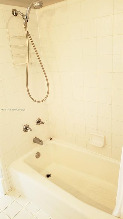 Bathtub enclosure featuring full-height ceramic wall tile, a handheld shower fixture, dual-handle controls, and an integrated recessed soap dish
