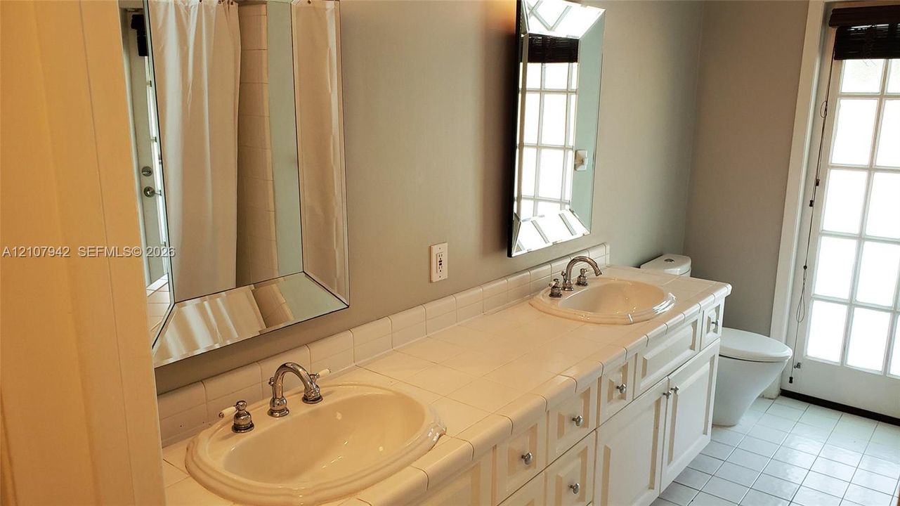 Double vanity with a tiled countertop, dual drop-in sinks, white cabinetry, beveled-edge mirrors, and a glass-paned door
