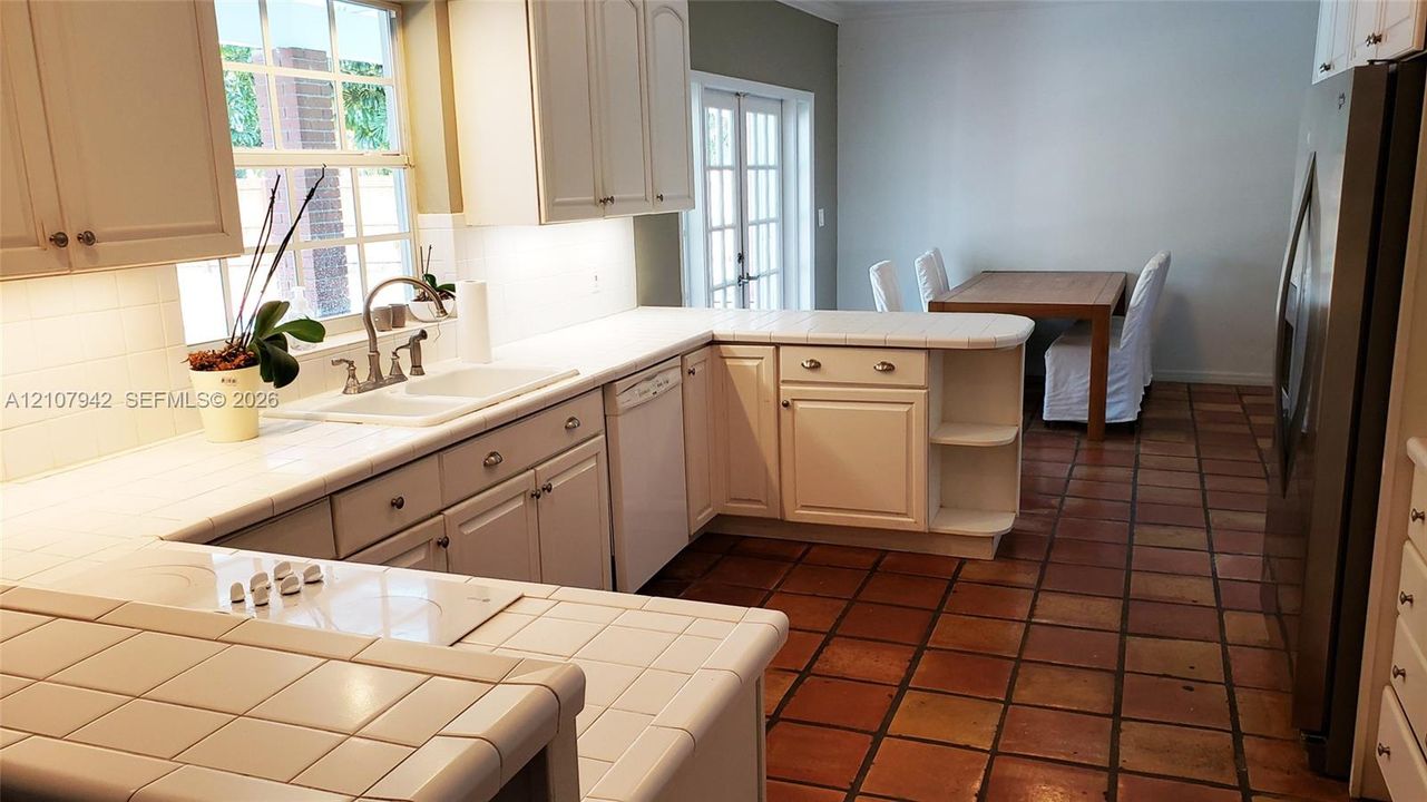 Kitchen featuring white cabinetry, tile countertops, integrated cooktop, stainless steel refrigerator, and terracotta-style tile flooring