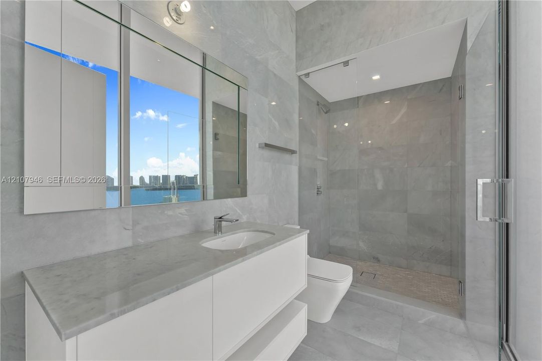 Bathroom featuring a floating vanity with a stone countertop, an integrated rectangular sink, wall-to-wall mirror, and a glass-enclosed shower with tiled flooring