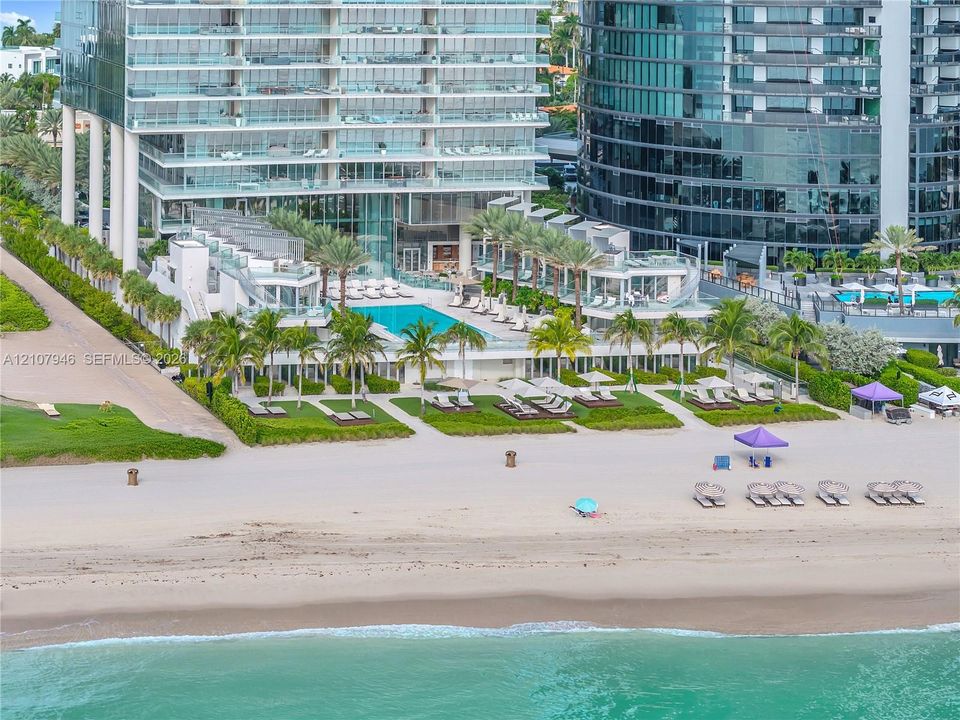 Beachfront high-rise property featuring a multi-level swimming pool, private coastal access, manicured landscaping, and glass-railed terraces