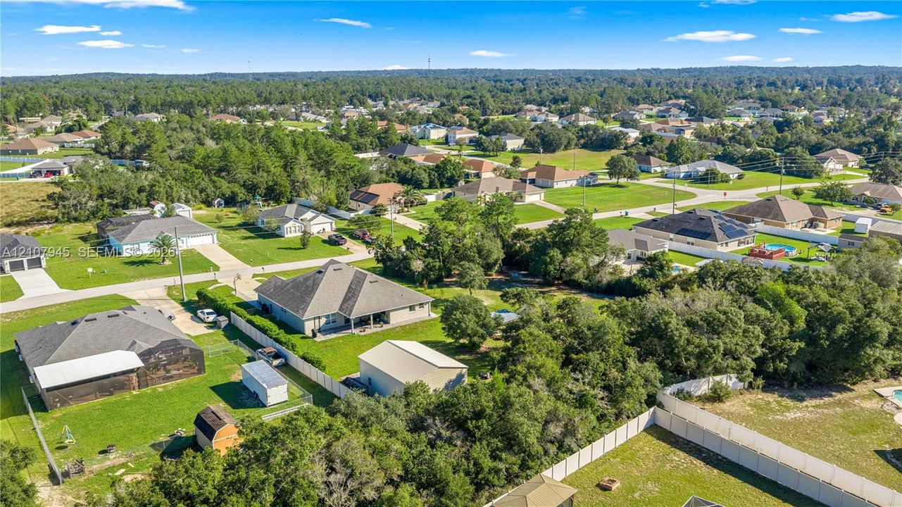 Aerial perspective of the property featuring a detached garage, expansive green space, mature trees, and perimeter fencing