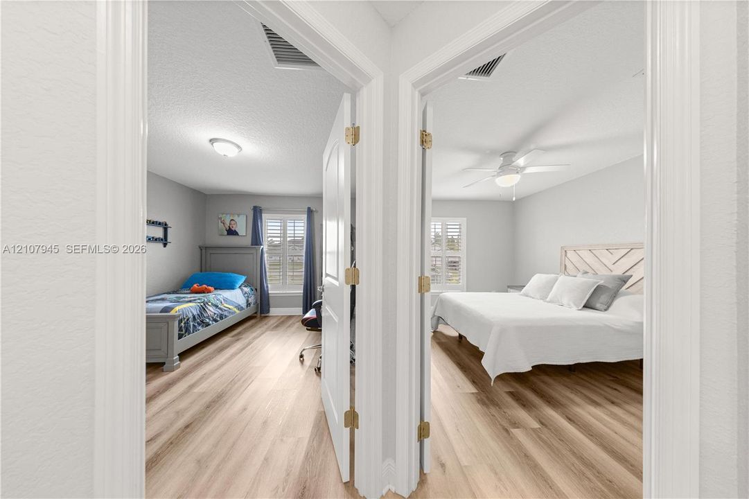 Dual rooms featuring wood-finish flooring, white paneled doors, ceiling fans, and interior window shutters