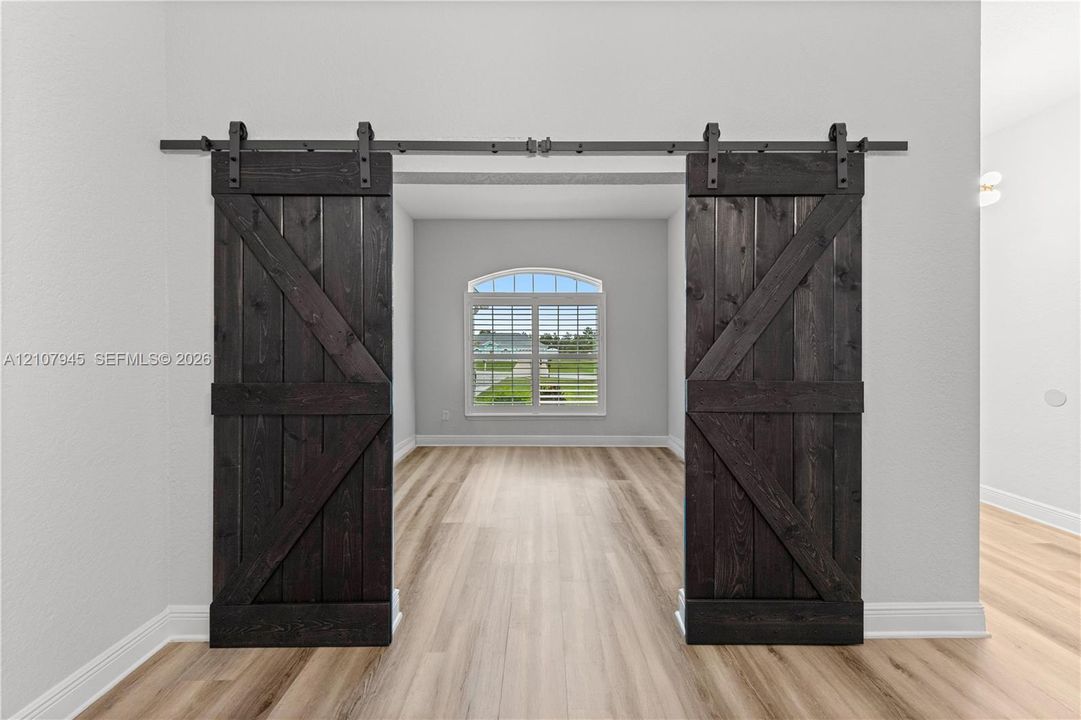 Dark-stained wood barn doors featuring matte black hardware, arched window with shutters, and wood-finish flooring