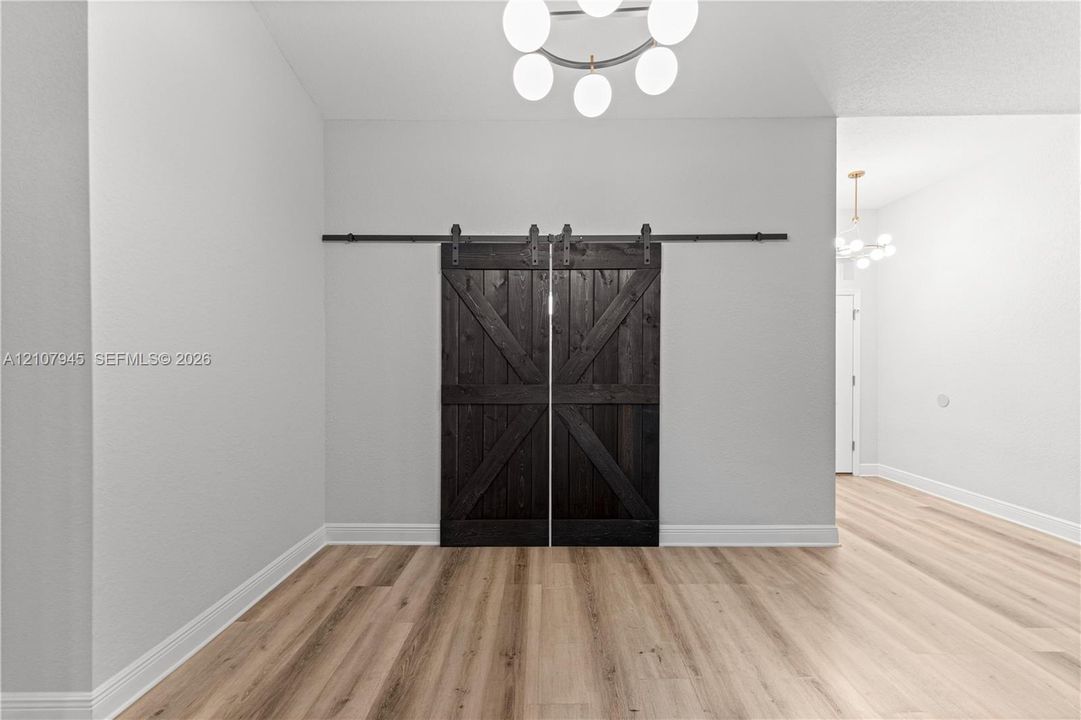 Double sliding barn doors with a dark wood finish and black hardware, complemented by wood-finish flooring and a multi-bulb geometric chandelier