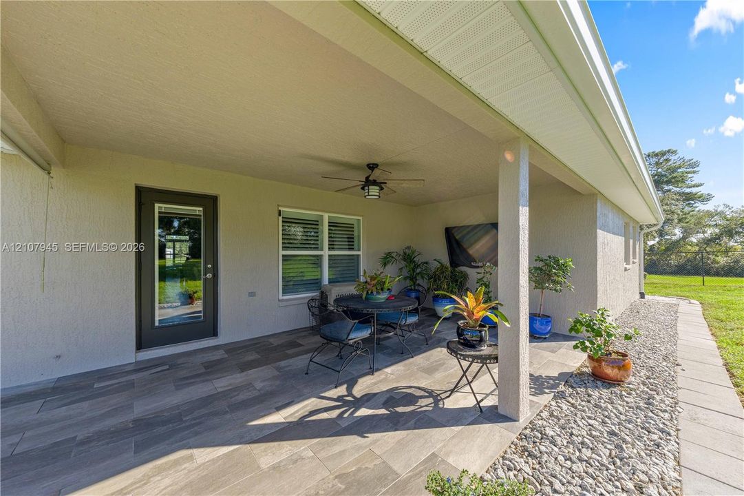 Covered outdoor patio featuring wood-finish tile flooring, a ceiling-mounted fan, and a glass-paneled exterior door