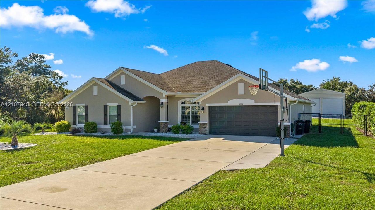 Single-story exterior featuring a neutral stucco facade, hip roof, multi-car garage, concrete driveway, and a detached structure