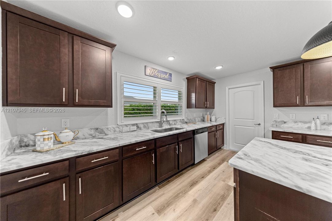 Kitchen featuring dark-finish cabinetry, stone-pattern countertops, stainless steel sink with pull-down faucet, wood-finish flooring, and recessed ceiling lighting