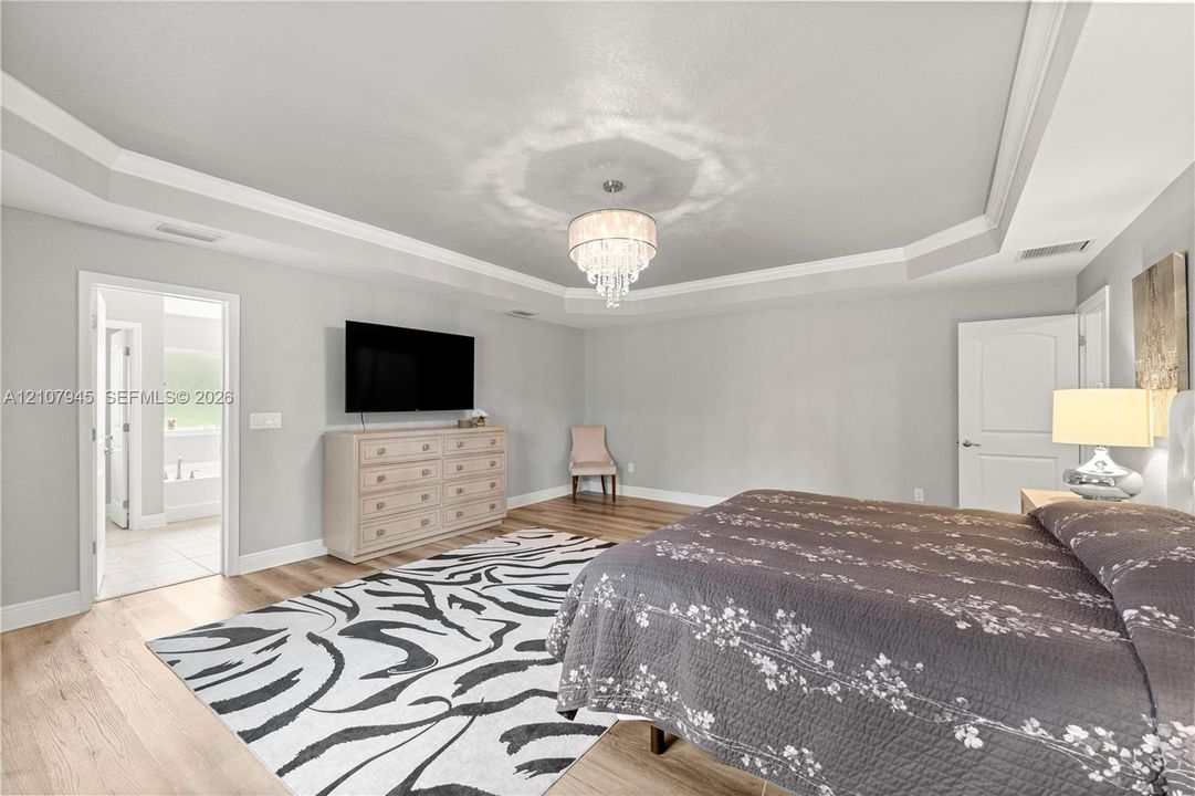 Tray ceiling with crown molding, crystal chandelier, wood-finish flooring, and solid-core interior doors