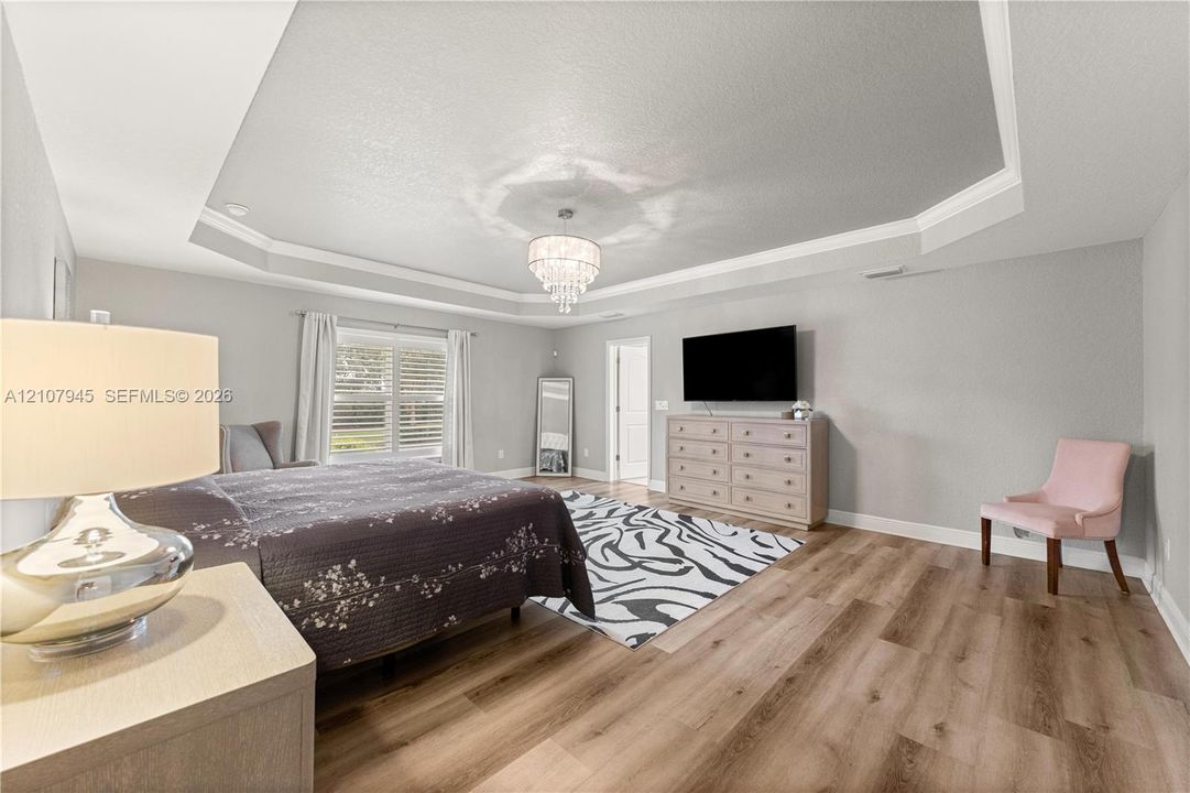 Tray ceiling with crown molding, wood-finish flooring, and a crystal chandelier