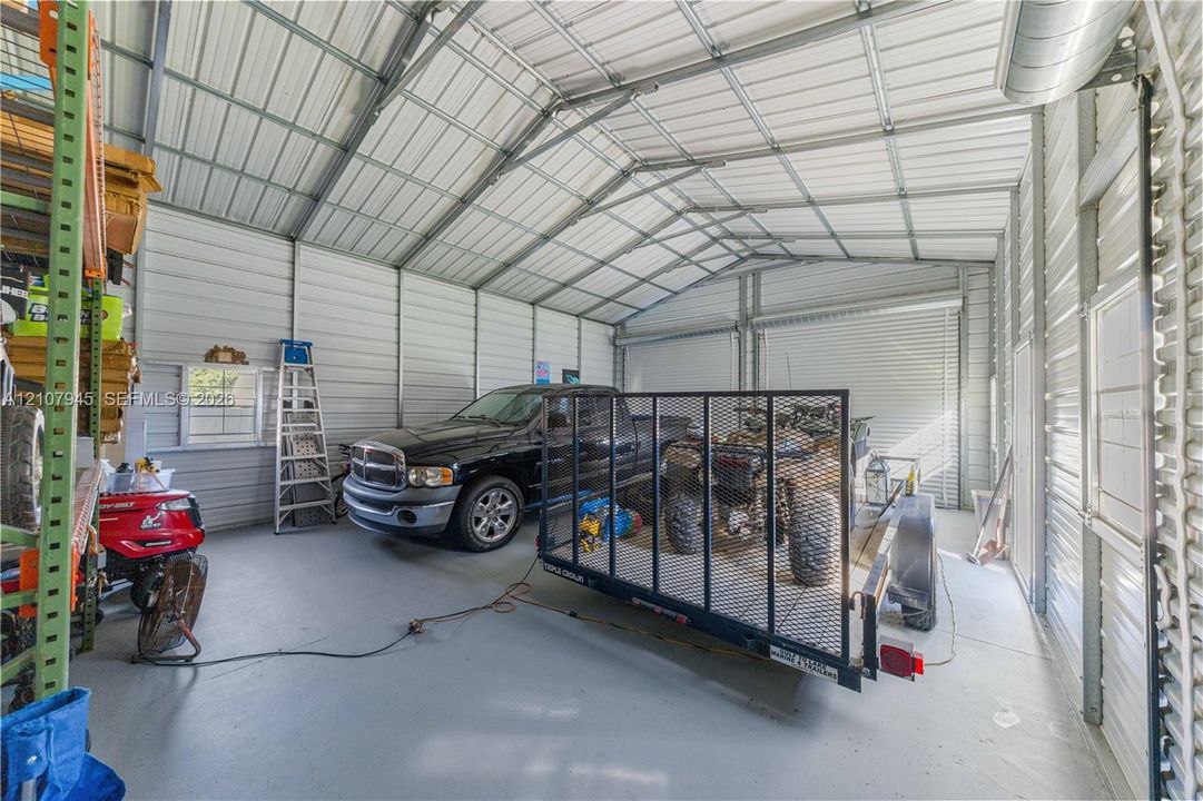Detached metal structure featuring a vaulted ceiling, finished concrete flooring, exposed steel framing, and a roll-up vehicle door