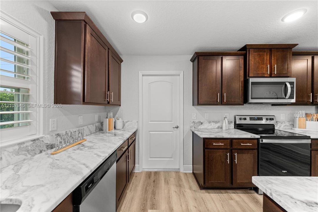 Kitchen featuring stained wood cabinetry, stone-patterned countertops, stainless steel appliances, wood-finish flooring, and shutter-style window treatments