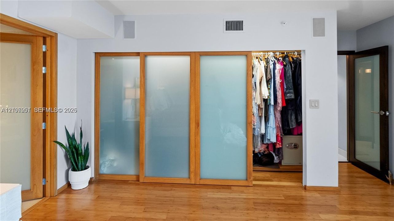 Custom millwork featuring floor-to-ceiling sliding closet doors with frosted glass panels and wood-finish trim, complemented by wood-finish flooring and a matching interior door frame
