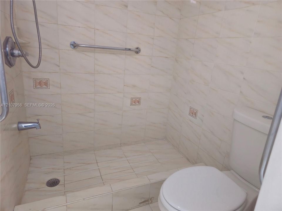 Walk-in shower enclosure featuring floor-to-ceiling tile, chrome plumbing fixtures, wall-mounted grab bars, and decorative accent tiles, paired with a standard-profile toilet