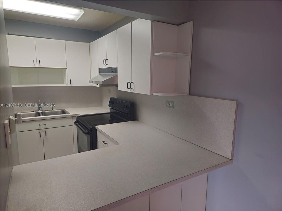 Kitchen featuring white cabinetry with open shelving, solid-surface countertops, dual-basin stainless steel sink, and integrated range hood