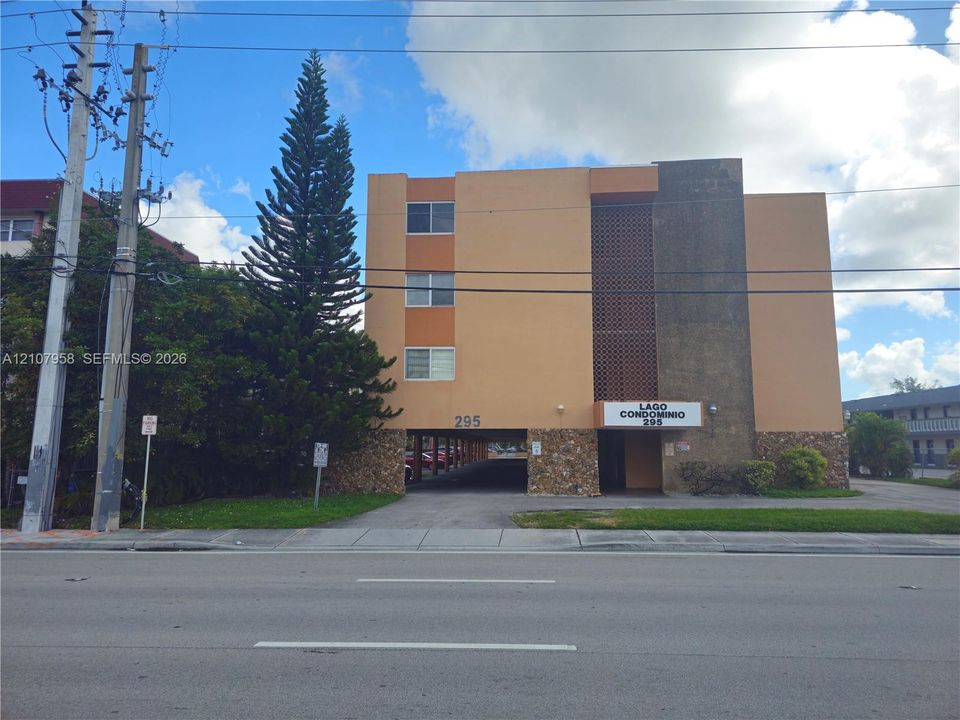 Multi-story condominium exterior featuring a stucco facade, stone veneer base, patterned masonry screening, and covered ground-level parking