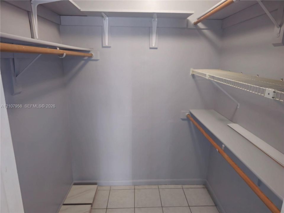 Walk-in closet featuring multi-level shelving, wood-finish clothing rods, and tile flooring