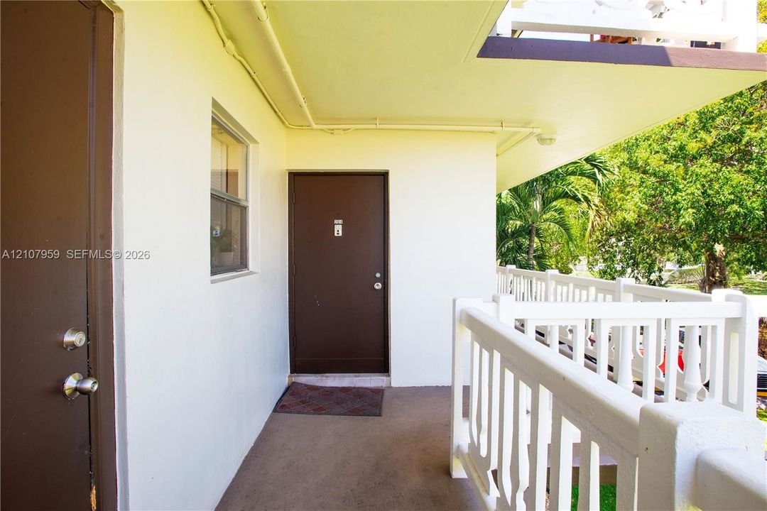Covered exterior walkway featuring a concrete floor, solid-core doors with metallic hardware, and a white balustrade railing
