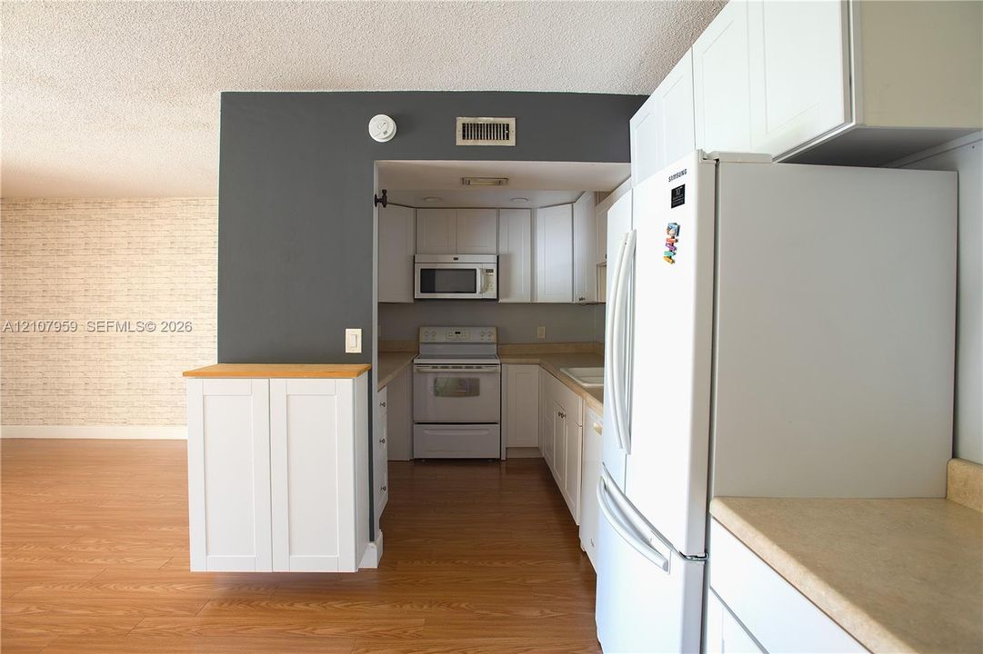 Kitchen area featuring white shaker-style cabinetry, wood-finish flooring, a built-in microwave, and a range