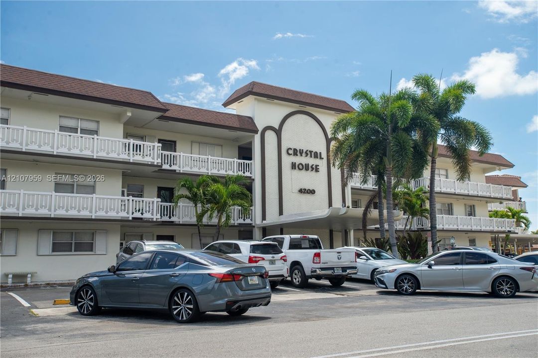 Multi-story exterior featuring a shingled roof, white balcony railings, a covered entrance portico, and integrated mature palm landscaping