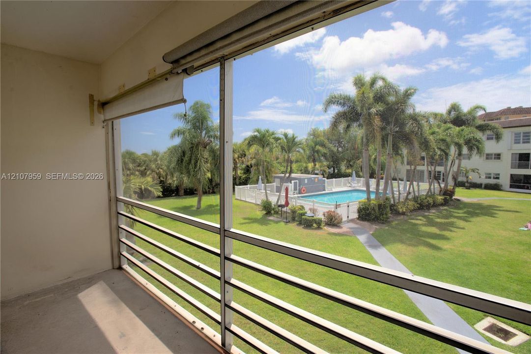 Screened-in balcony featuring metal railing, outdoor pool, paved walkway, and landscaped grounds
