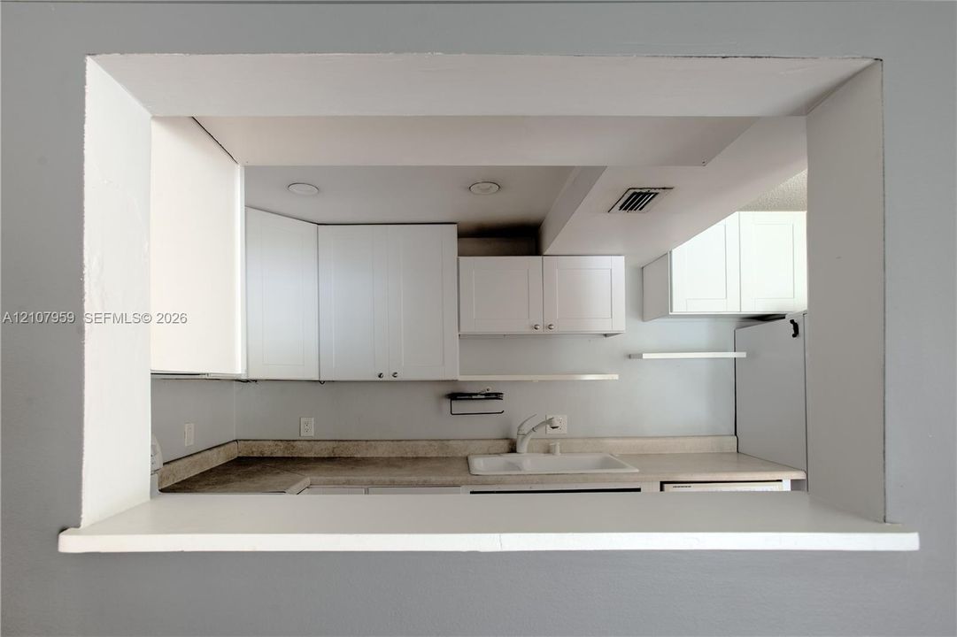 Pass-through opening featuring white cabinetry, solid-surface countertops, recessed lighting, and a white sink