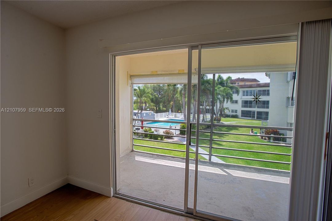 Sliding glass door opening to a private balcony featuring metal railings, wood-finish flooring, and exterior exposure to a swimming pool and landscaped grounds
