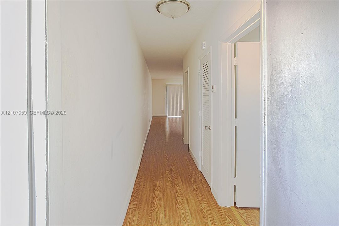 Hallway featuring wood-finish flooring, flush-mount ceiling lighting, and louvered closet doors