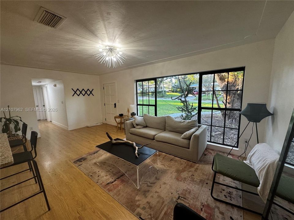 Living area featuring large windows with black metal frames, wood-finish flooring, and a contemporary sunburst-style overhead light fixture
