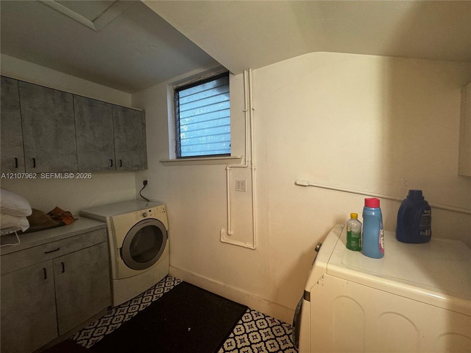 Laundry area featuring built-in cabinetry with stone-finish surfaces and a window with horizontal security bars
