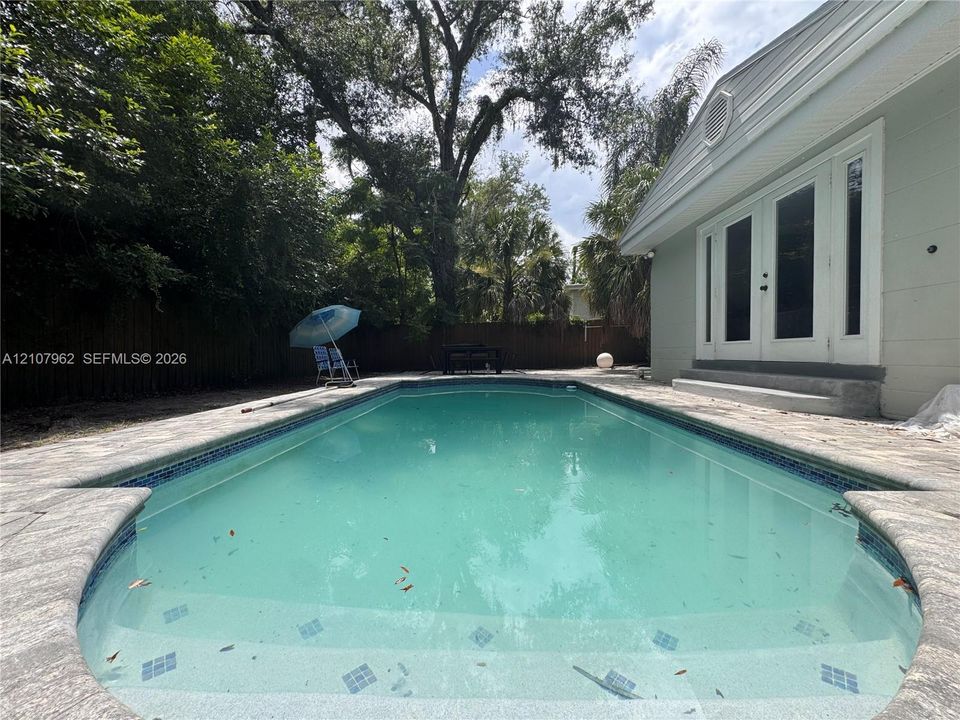 Rectangular in-ground swimming pool with stone-finish decking, light-colored siding, and dual glass-panel exterior doors