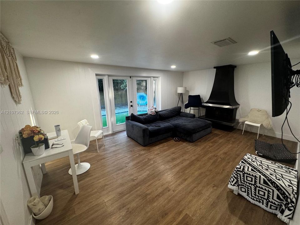 Living area featuring wood-finish flooring, recessed lighting, double glass doors, and a black metal fireplace