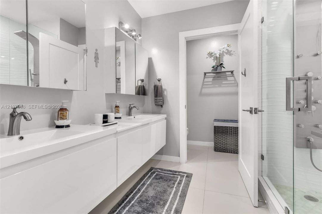 Dual-sink floating vanity with white cabinetry, integrated rectangular basins, and brushed-nickel faucets, complemented by a walk-in glass shower featuring multiple body spray jets and a tiled floor