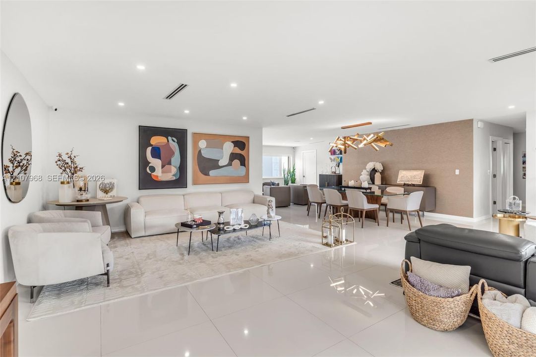 Open-concept interior featuring large-format tile flooring, recessed ceiling lighting, textured accent wall, and a contemporary multi-arm chandelier